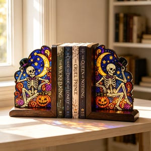 May include: A pair of dark wood bookends featuring stained glass panels with a skeleton wearing a top hat, a crescent moon, stars, and a jack-o'-lantern. The books titled The Wicked King, A Curse So Dark and Lonely, The Cruel Prince, and The Queen of Nothing are held between them.