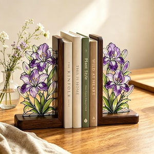 May include: A pair of L-shaped dark wood bookends featuring decorative stained glass panels with purple iris flowers and green leaves. The bookends support four books titled The Kinfolk Home, This Is Home, Plant Style, and Wild at Heart.