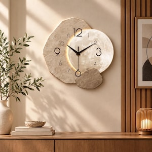 May include: A wall clock featuring an irregular, textured beige stone-like backing and a circular, illuminated moon-patterned face. The clock has black hands and black numerals for 1, 2, 3, 4, 5, 7, 8, 9, 10, 11, and 12, with a circular pendulum.