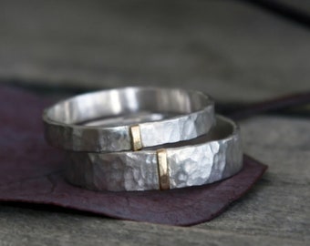May include: Two silver rings with a hammered, textured finish. Each band features a single, vertical, smooth gold-colored inlay segment that interrupts the hammered pattern, creating a contrast between the silver and gold elements.