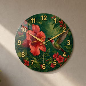 May include: A round wall clock featuring a vibrant illustration of a hummingbird hovering near a large red hibiscus flower. The clock face has a dark green background with gold-colored numerals from 1 to 12 and thin gold-colored clock hands.