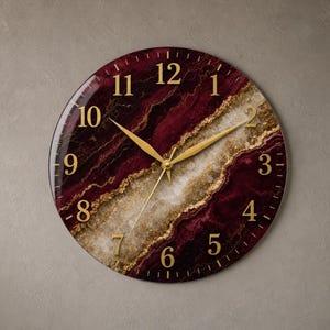 May include: A round wall clock featuring a deep burgundy and white marbled pattern with gold-colored veins. The clock face displays gold-colored Arabic numerals from one to twelve and matching gold-colored hour, minute, and second hands.