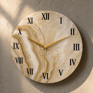 May include: A round wall clock featuring a beige and cream agate-inspired pattern with swirling textures and gold-toned accents. The clock face displays black Roman numerals from I to XII and includes thin, pointed gold-colored hour and minute hands.
