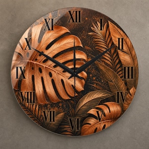 Pode incluir: Um relógio de parede redondo com fundo escuro e folhas tropicais de monstera e palmeira em tons de cobre. O mostrador exibe algarismos romanos pretos de I a XII e inclui dois ponteiros pretos finos centralizados para marcar as horas.