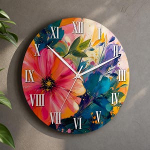 Pode incluir: Um relógio de parede redondo com uma pintura floral abstrata vibrante com grandes pétalas cor-de-rosa, laranja e azuis. O mostrador exibe algarismos romanos brancos de I a XII dispostos em círculo, com ponteiros brancos finos no centro.
