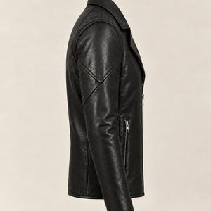 May include: A black jacket with a textured finish, featuring a notched collar, long sleeves with stitched panel detailing, and a vertical zippered pocket on the side. The garment is shown from a side profile view, highlighting the structured seams.