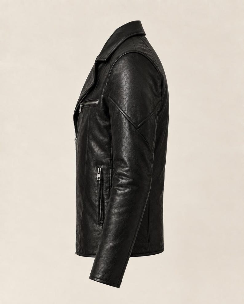 May include: A black jacket with a textured finish, featuring a notched collar, long sleeves, and silver-toned metal zippers on the front chest and side pockets. The garment is shown from a side profile view, highlighting the structured shoulder seams.