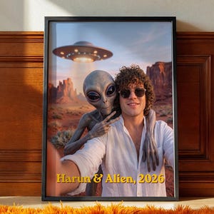May include: A framed print featuring a selfie of a person with curly hair wearing sunglasses and a white shirt alongside a grey alien. In the background, a UFO hovers over a desert landscape. The text 'Harun & Alien, 2026' is printed in yellow.
