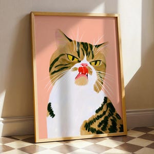 Puede incluir: Una impresión de arte mural enmarcada que presenta una ilustración digital de un gato atigrado marrón y blanco con expresión gruñona, ojos amarillos y la lengua rosa fuera, sobre un fondo liso de color melocotón claro en un marco de madera.