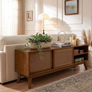 May include: A rectangular wooden media console featuring two sliding doors with woven cane panels, supported by four tapered legs. The unit includes an open shelving section on the right side, providing storage space for books and decorative items.