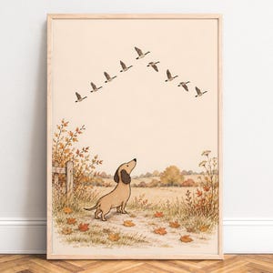 Op de afbeelding: Een ingelijste muurkunstprint met een beige teckel die op een pad staat dat bedekt is met gevallen oranje en bruine herfstbladeren. De hond kijkt omhoog naar een V-vormige formatie van acht ganzen die door een bleke crèmekleurige lucht boven een landelijk landschap vliegen.