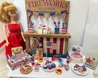 May include: A miniature Fourth of July display featuring a doll in a red dress, a fireworks stand, and various patriotic treats. The stand has a sign that reads "FIREWORKS SOLD HERE" and is decorated with American flags and bunting. Cakes, cookies, and drinks are decorated with red, white, and blue.