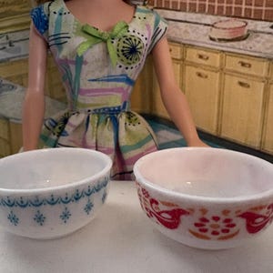 May include: Two white ceramic bowls. One bowl has a blue floral pattern, and the other has a red and orange bird and floral design. The bowls are on a white surface.
