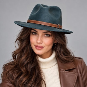 May include: A dark teal fedora hat featuring a structured crown and a wide brim. The hat is accented with a thin, smooth brown leather band that encircles the base of the crown, providing a distinct contrast to the deep teal color of the hat.