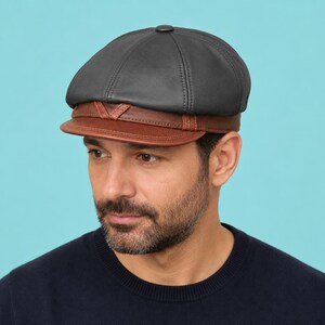 May include: A newsboy cap featuring a dark charcoal grey leather crown with stitched paneling and a contrasting brown leather brim. The cap includes a decorative brown leather band detail across the front, just above the stiff, curved visor.