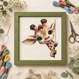 May include: A square cross-stitch embroidery featuring a cartoon giraffe peeking from behind a vertical line, framed in a green wooden border. The giraffe has large dark eyes, brown spots, and small horns, set against a white fabric background.