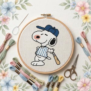May include: A cross-stitch embroidery project in a wooden hoop featuring a white cartoon dog wearing a blue baseball cap and a blue-and-white striped shirt, holding a wooden baseball bat, surrounded by embroidery floss and metal scissors.