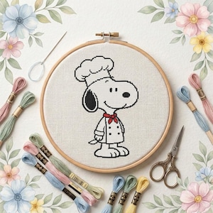 May include: A cross-stitch project in a wooden embroidery hoop featuring a black and white Snoopy character wearing a chef hat and a red neckerchief. The kit includes embroidery floss in pastel colours, a silver needle, and vintage-style scissors.