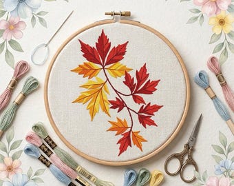 May include: A circular wooden embroidery hoop containing a fabric panel with a stitched design of maple leaves in shades of red, orange, and yellow. The set includes a silver needle, vintage-style metal scissors, and several skeins of embroidery floss.