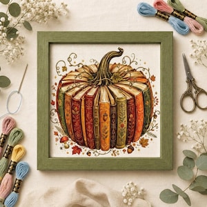 May include: A square cross-stitch embroidery in a green wooden frame featuring a pumpkin shape constructed from vertically arranged vintage books with ornate spines, surrounded by small autumn leaves, mushrooms, acorns, and swirling vine motifs.