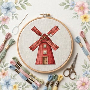 Könnte beinhalten: Ein Kreuzstichprojekt in einem hölzernen Stickrahmen mit einer roten Windmühle mit vier Flügeln, einer zentralen Tür und zwei Fenstern. Der Rahmen ist von mehreren bunten Stickgarnsträngen, einer silbernen Nadel und einer Schere umgeben.