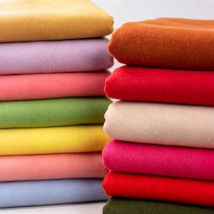 May include: Two stacks of folded fabric sheets in a variety of solid colours including mustard yellow, lavender, coral, light green, bright yellow, pale pink, light blue, burnt orange, red, cream, magenta, deep red, and dark olive green.