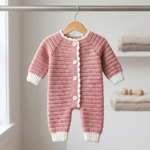 May include: A dusty rose crochet romper featuring long sleeves with white ribbed cuffs, a round neckline with a white scalloped trim, and a front button closure with four white buttons. The garment is displayed on a wooden hanger.