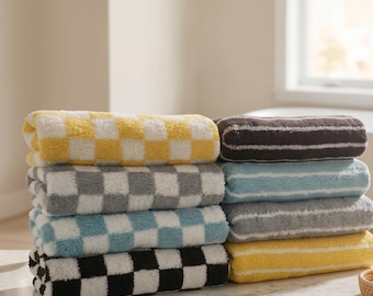 May include: A stack of eight folded towels arranged in two columns. The left column features four towels with a checkered pattern in yellow, gray, blue, and black. The right column features four towels with horizontal stripes in brown, blue, gray, and yellow.