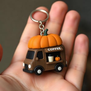 Op de afbeelding: Een bruine koffiewagen-sleutelhanger met een grote oranje pompoen op het dak. De zijkant van de wagen heeft een uitgiftevenster met het woord COFFEE erboven, een klein wit bekertje en een piepklein pompoentje op de toonbank.