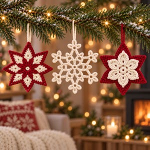 May include: Three crocheted ornaments hanging from a pine branch. The left ornament is a red and cream star, the center is a cream snowflake, and the right is a red star with a cream flower center. Each piece features a matching hanging loop.