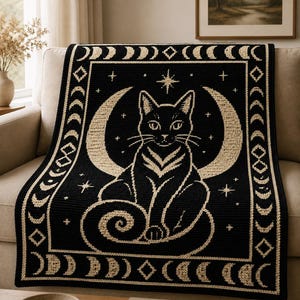 Könnte beinhalten: Eine schwarz-cremefarbene Strickdecke mit einem zentralen Motiv einer Katze, die vor einem Halbmond sitzt. Der Rand ist mit einem sich wiederholenden Muster aus Mondphasen, Sternen und Rauten in einer Kontrastfarbe verziert.