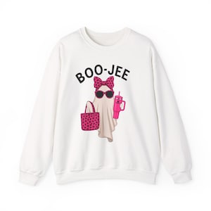 May include: A white long-sleeve sweatshirt featuring a graphic of a ghost wearing a pink leopard print bow and sunglasses. The ghost holds a pink tote bag with a matching leopard print and a pink tumbler. The text BOO-JEE is printed in black above.