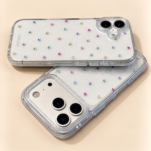 May include: Two clear smartphone cases featuring a glittery finish and scattered small multi-colored star icons. Each case has a reinforced camera cutout area and visible side buttons, designed to protect the device while maintaining a transparent look.
