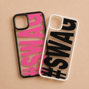 May include: Two rectangular phone cases, one with a black frame and hot pink text reading #SWAG, and the other with a white frame and black text reading #SWAG. Both cases feature a transparent center section and a cutout for a camera lens.