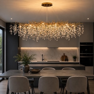 May include: A large, horizontal, gold-toned chandelier featuring a branch-like frame adorned with numerous clear, teardrop-shaped crystal pendants that hang at varying lengths, creating a dense, cascading effect over a dining area.