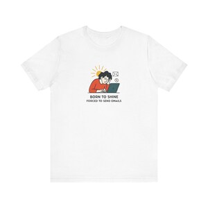 May include: A white short-sleeve t-shirt featuring a graphic of a person working on a laptop with a sun icon, an envelope, and a clock. Below the graphic, the text reads: BORN TO SHINE FORCED TO SEND EMAILS in black, capitalized, sans-serif font.