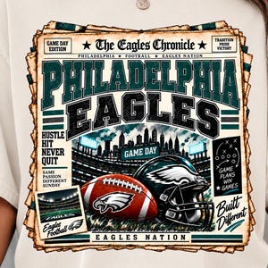 Może przedstawiać: Kremowy t-shirt z nadrukiem graficznym zatytułowanym The Eagles Chronicle. Projekt zawiera napis Philadelphia Eagles, piłkę do futbolu amerykańskiego, kask, scenę stadionową oraz różne hasła, takie jak Hustle Hit Never Quit i Built Different.