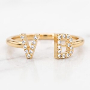 Peut inclure: Une bague ouverte en or avec les lettres V et B comme points centraux. La lettre V est incrustée de petites pierres claires, et la lettre B est également incrustée de petites pierres claires. L'anneau est en or lisse et poli.