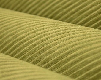 May include: A close-up view of olive green corduroy fabric featuring distinct, raised vertical ridges or wales running diagonally across the surface. The material has a soft, textured appearance with a consistent color throughout the textile.