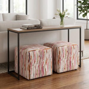 May include: A rectangular console table with a thin black metal frame and a wood-grain top, featuring two square ottomans upholstered in a cream fabric with vertical, multi-colored stripes in shades of red, orange, yellow, and blue.