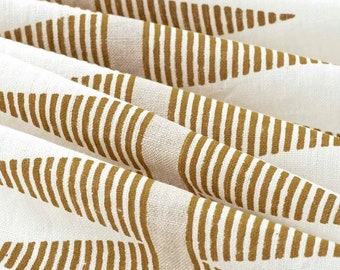 May include: Close-up of a folded white fabric with a repeating pattern of brown vertical lines and arrow-shaped designs. The fabric has a textured appearance, with visible weave details. The pattern is evenly spaced across the surface.