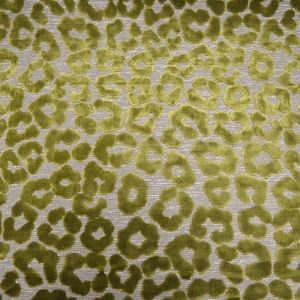 May include: A textile fabric featuring a raised, velvet-like texture in a vibrant olive green color. The surface displays a repeating, irregular leopard-style spot pattern set against a neutral, light-colored woven background base.
