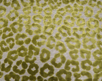 May include: A fabric featuring a repeating leopard print pattern in olive green velvet against a light gray textured background. The soft, raised velvet spots create a distinct contrast with the woven base, forming a dense, organic animal-inspired design across the entire surface of the material.