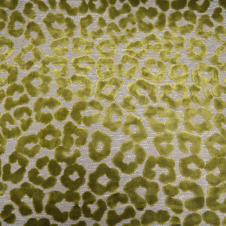 May include: A textile fabric featuring a raised, velvet-like texture in a vibrant olive green color. The surface displays a repeating, irregular leopard-style spot pattern set against a neutral, light-colored woven background base.