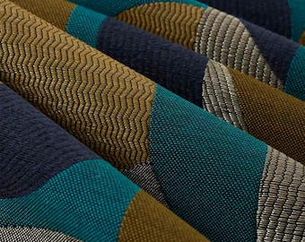 May include: A woven fabric featuring a geometric pattern of overlapping circles and diagonal bands. The textile displays a color palette of deep navy blue, vibrant teal, muted olive green, and metallic silver, with a distinct chevron texture.