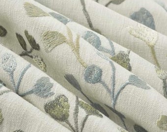 May include: Off-white fabric featuring an embroidered botanical pattern with stems and rounded buds in shades of sage green, olive green, and dusty blue. The textile has a visible woven texture and is draped to create soft, deep folds.