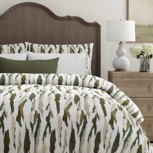 Puede incluir: Un juego de cama que incluye una funda n&oacute;rdica blanca y fundas de almohada a juego con un patr&oacute;n abstracto de pinceladas verticales en tonos verde oliva, verde bosque oscuro y beige. Un coj&iacute;n rectangular verde oliva liso se sit&uacute;a delante.