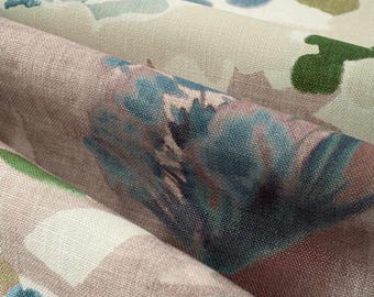 May include: A folded piece of fabric featuring a watercolor-style floral pattern in shades of blue, green, and brown on a light beige background. The textile has a visible woven texture with soft, blended edges between the colorful shapes.