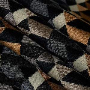 Puede incluir: Primer plano de una tela con un patr&oacute;n geom&eacute;trico. El dise&ntilde;o presenta un patr&oacute;n de diamantes repetidos en tonos negro, gris, beige y dorado. La tela parece texturizada, con detalles de tejido visibles y pliegues.