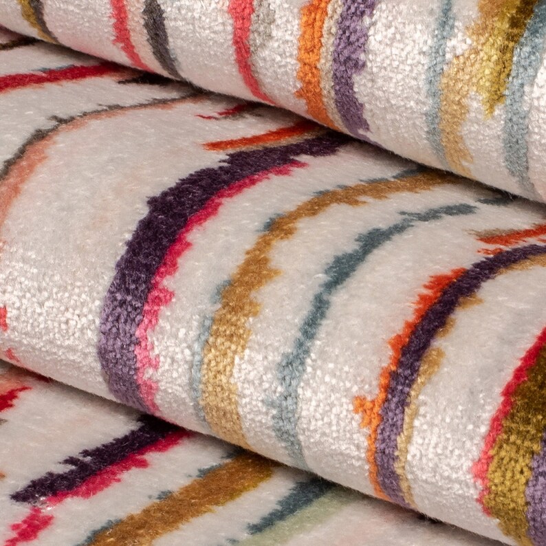 May include: A white fabric featuring a textured, multi-colored pattern of wavy, vertical stripes in shades of purple, orange, pink, teal, and gold. The material has a soft, plush appearance with distinct, irregular lines running across the surface.